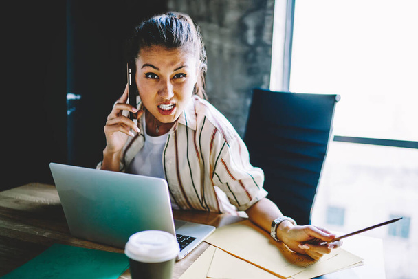 Angry business woman raging during mobile phone conversation upset with wrong service, irritated female employee sitting at desktop making smartphone call for discussing problems during wor - Foto, Bild