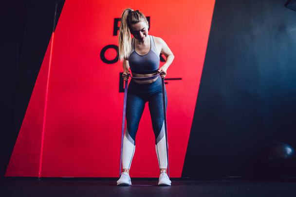 Fitness woman bodybuilder holding expander for training muscles enjoying time for weight loss in sport gym, attractive Caucasian female athlete using elastic rubber during workout indoors - Fotografie, Obrázek