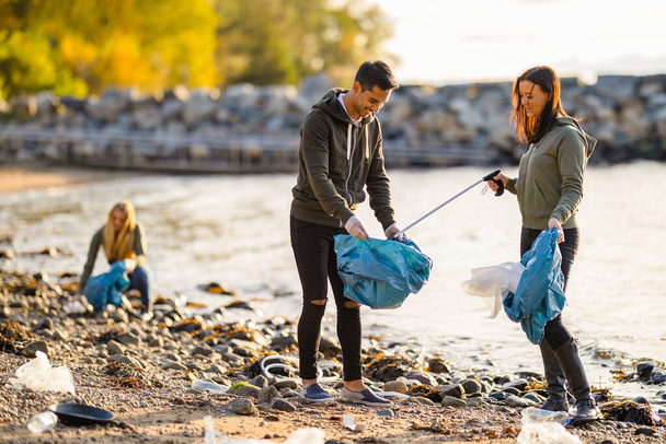Ryhmä vapaaehtoisia puhdistamassa rantaa aurinkoisena päivänä
 - Valokuva, kuva