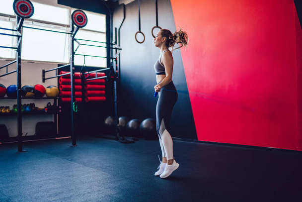 Concentrated fitness girl skipping rope for training and warming up body muscules spending day for workout in gym, attractive woman with slim figure jumping with equipment making effort indoors - Foto, Imagem