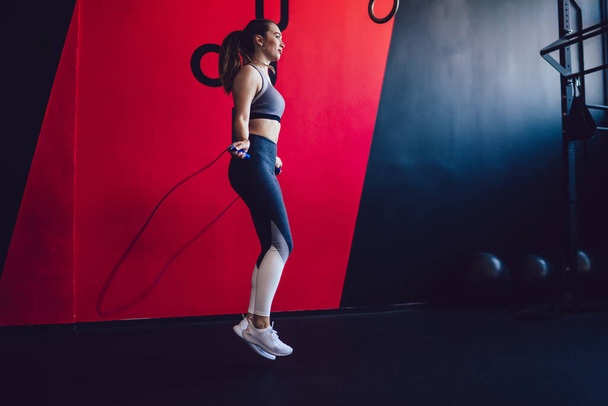 Young woman with rope skipping during workout time in modern pilates studio concentrated on physical training for slimming, attractive active hipster girl in sportswear jumping for weight loss - Photo, Image