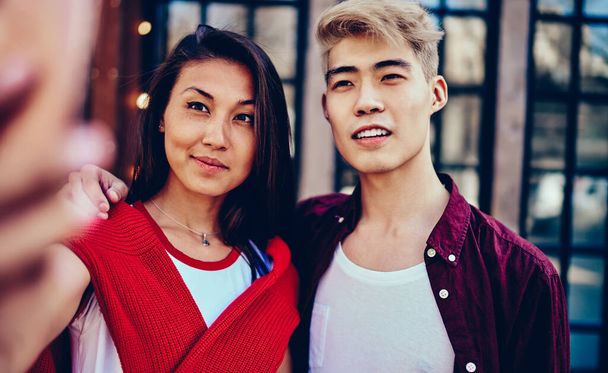 Chinese hipster guy hugging asian girlfriend during meeting outdoors in urban setting.Attractive japanese couple in love standing on street and spending free time together - 写真・画像