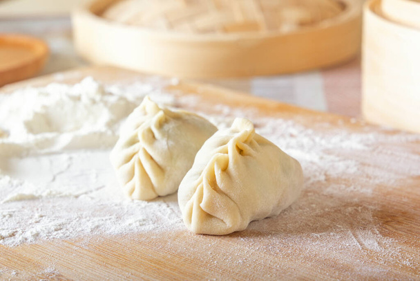 Raw manti, dumplings or wonton from dough with minced meat filling on the kitchen table with flour on a background of a wooden double boiler. Homemade food. Close-up. - 写真・画像