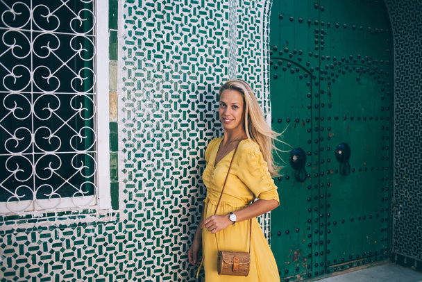 Half length portrait of beautiful woman in yellow sundress posing near bohemian fresco architecture enjoying summer vacation in Morocco, hipster girl spending holidays for discover berber culture - Fotografie, Obrázek