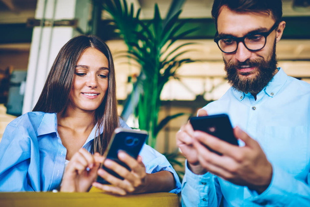 Happy male and female holding smartphone devices and messaging with friends ignoring live communication, man and woman using digital gadgets for updating profiles in social networks during free time - Φωτογραφία, εικόνα