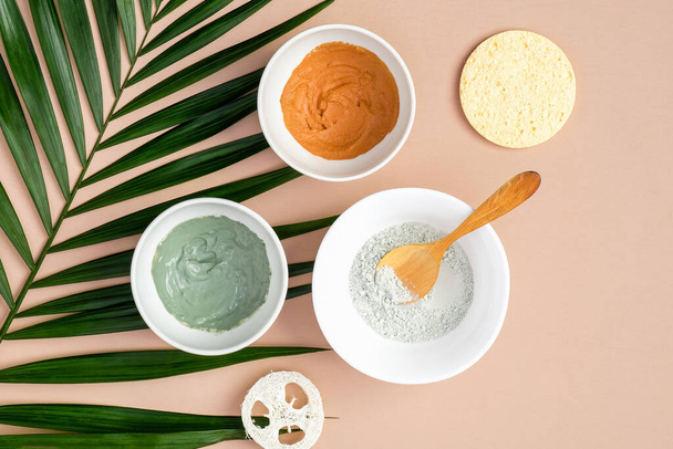 Bowls with clay masks for face treatment with tropical palm leaf on brown background, top view. Facial skincare concept - Φωτογραφία, εικόνα