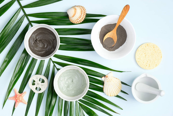 Face clay masks in bowls with tropical palm leaf, top view. Facial skincare, SPA natural organic cosmetic concept - Fotó, kép
