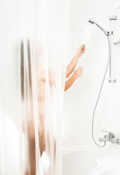 Brunette nainen pesu suihkussa takana läpinäkyvä verho
 - Valokuva, kuva