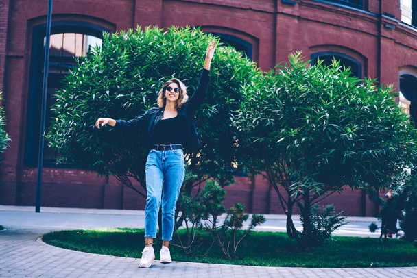 Full length portrait of joyful hipster girl dressed in casual look having fun on urban setting during sunny spring day, successful female teenager in sunglasses looking at camera and enjoying weekend - Foto, Imagen