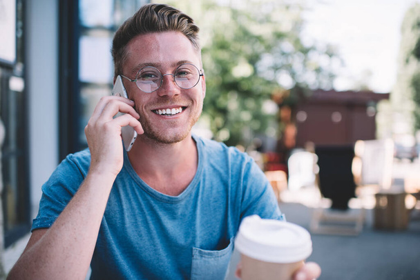 Rejoice hipster guy in classic glasses looking at camera and smiling happy from good roaming internet connection on cellphone, cheerful man excited with phone call and time for talking with friend - Zdjęcie, obraz