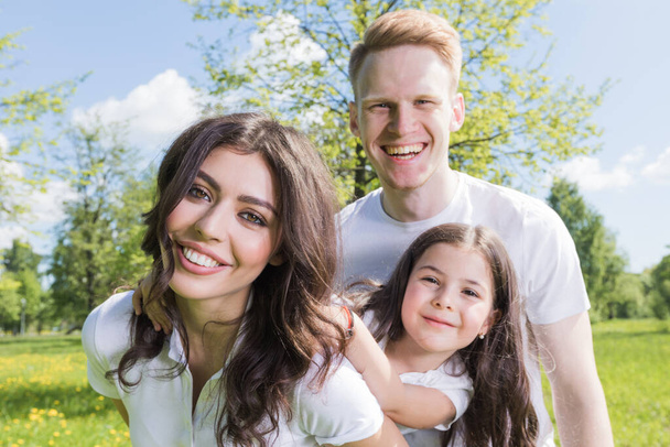 Happy family having fun outdoors in spring park against natural green meadow and trees background - Photo, Image