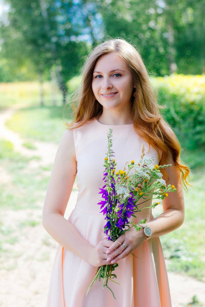 Lovely young girl with the flower bouquet at the nature park - Zdjęcie, obraz