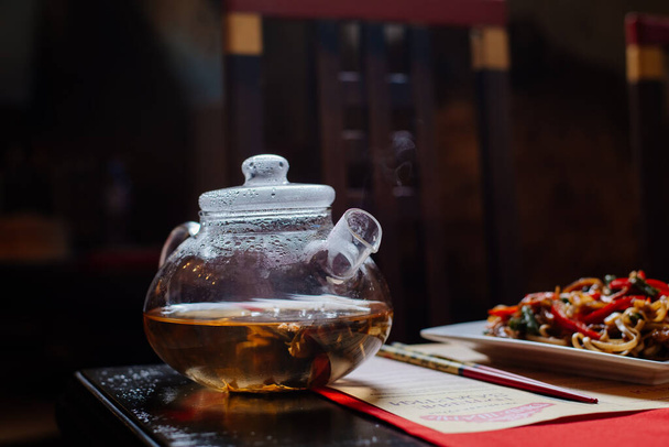 a glass teapot in which Chinese green tea is brewed. Steam comes from the spout of the kettle - Valokuva, kuva