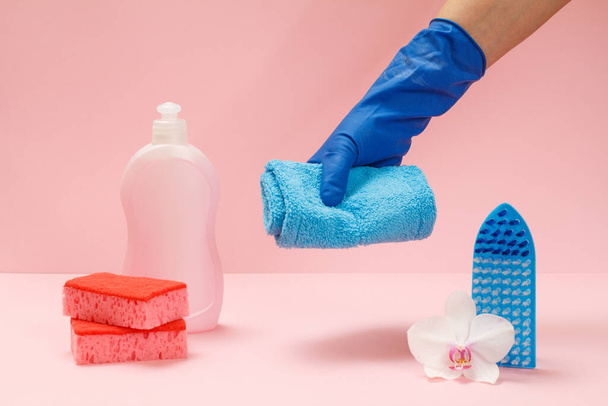 Műanyag flakon mosogatószer, szivacs, kefe és kéz egy gumikesztyűben, egy rongyot tartva a rózsaszín háttéren. Mosó- és tisztítókészlet. - Fotó, kép