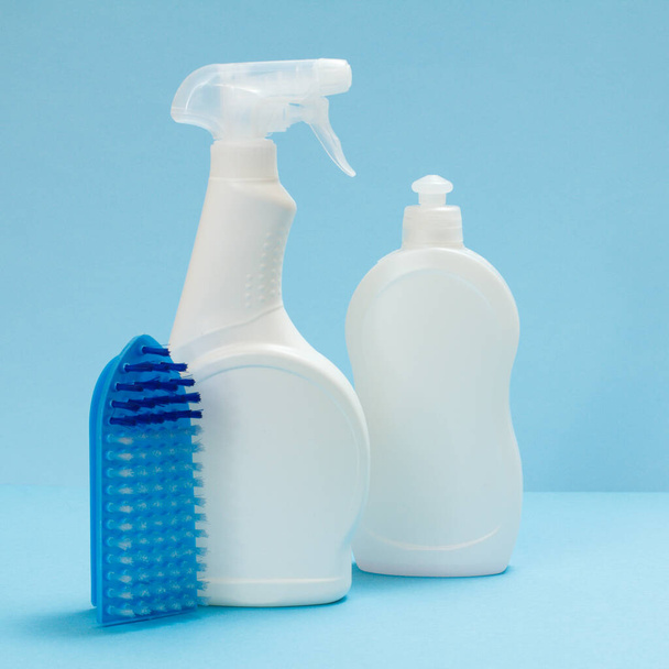 Plastic flessen afwasmiddel, glas en tegelreiniger en een borstel op de blauwe achtergrond. Was- en reinigingsset. - Foto, afbeelding