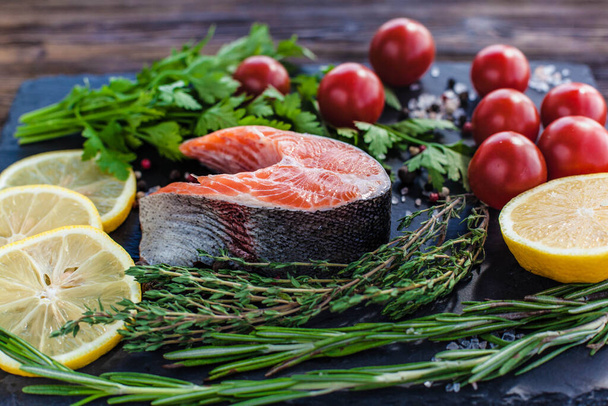 One salmon steak with greenery, lemon and cherry tomatoes on the black board - Photo, Image
