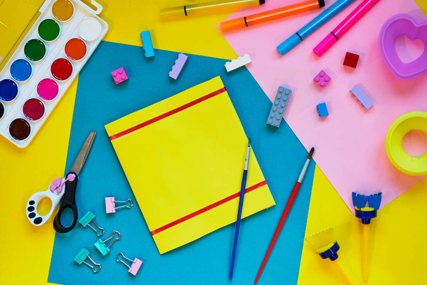 Schulbedarf, Schreibwaren auf gelbem Hintergrund - Platz für Bildunterschriften. Kind bereit, mit Bleistiften zu zeichnen und Anwendung von buntem Papier zu machen. Ansicht von oben. - Foto, Bild