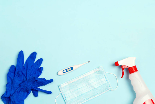 Protección contra el Coronavirus: guantes, mascarilla médica, antiséptico y termómetro sobre fondo azul. Concepto de enfermedad viral. Vista superior con espacio de copia
. - Foto, imagen