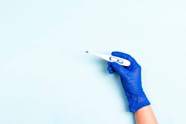Kéz a kézben kék orvosi kesztyű tartja a digitális hőmérő kék alapon. Megelőzés a vírustól. A szöveg másolási helye. - Fotó, kép