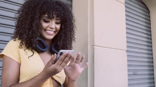 Stylish curly woman using smartphone posing on city background - Záběry, video