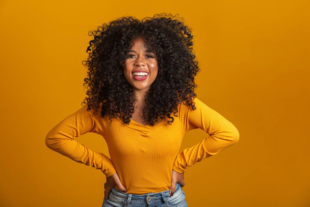 Mladá afro-americká žena s kudrnatými vlasy, dívá se do kamery a usmívá se. Roztomilé afro dívka s kudrnaté vlasy usmívající se na kameru. - Fotografie, Obrázek