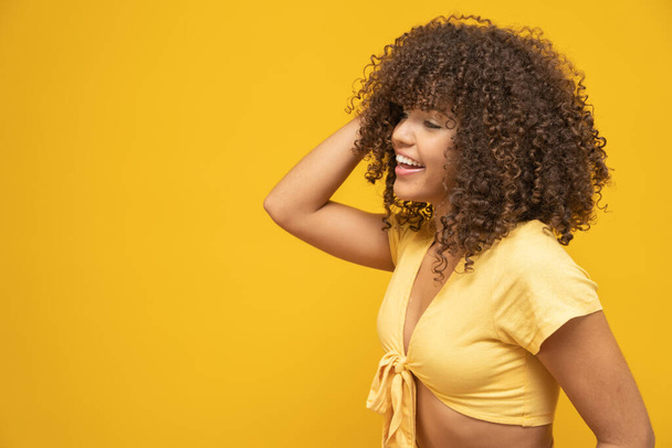 Nuori latino kihara nainen poseeraa kirkkaan keltaisella taustalla
 - Valokuva, kuva