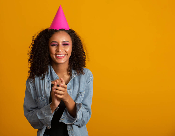 Young afro american woman wearing birthday hat over isolated yellow background with a happy and cool smile on face. Lucky person. - Photo, Image
