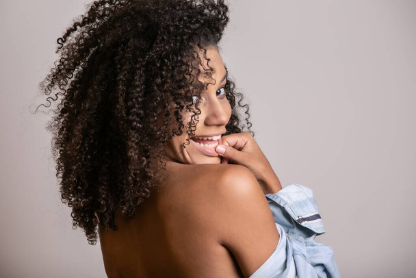 Mujer afroamericana joven con el pelo rizado mirando a la cámara y sonriendo. Linda chica afro con el pelo rizado sonriendo mirando a la cámara
. - Foto, Imagen
