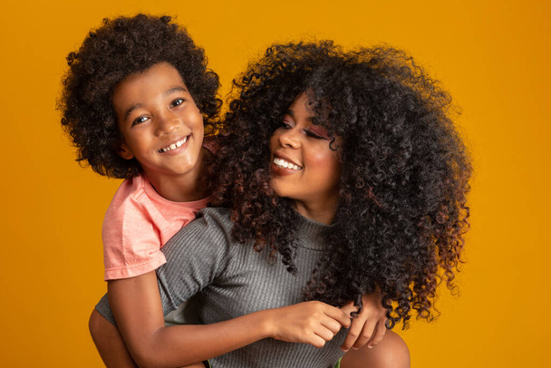 Portrait of young African American mother with toddler son. Yellow background. Brazilian family. - Фото, изображение