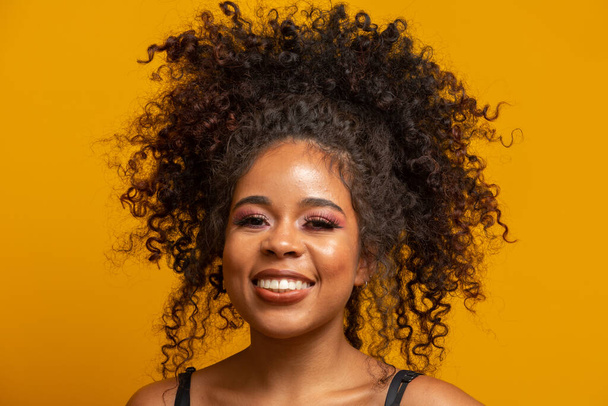 Krásný portrét africké americké ženy s afro účesem a půvabným make-upem. Brazilka. Míchaná rasa. Vlnité vlasy. Styl vlasů. Žluté pozadí. - Fotografie, Obrázek