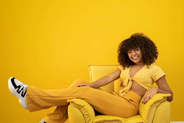 Nuori latino kihara nainen poseeraa kirkkaan keltaisella taustalla
 - Valokuva, kuva