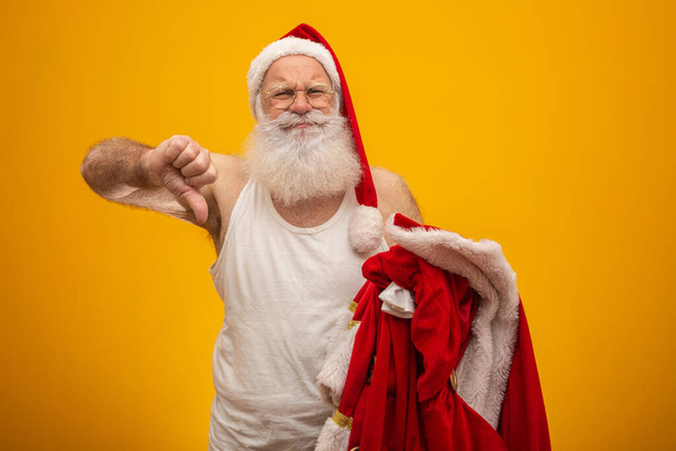 Der unglückliche Weihnachtsmann hält seine Kleidung nach oder vor der Bescherung in der Hand. Weihnachtsmannkleidung. Kostüm. Daumen runter. - Foto, Bild