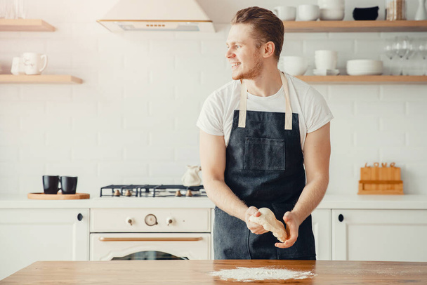 ダークエプロンで男性シェフイタリア料理は、軽量キッチンの背景にピザを焼くための生地を準備 - 写真・画像