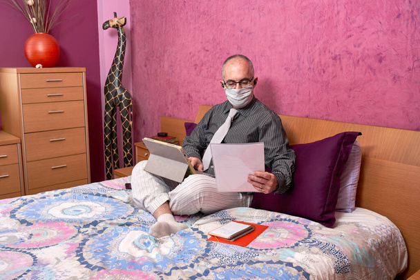 Geschäftsmann arbeitet von zu Hause aus, im Zimmer, mit dem Laptop, mit Hemd und Krawatte und Schlafanzug und Maske auf. - Foto, Bild