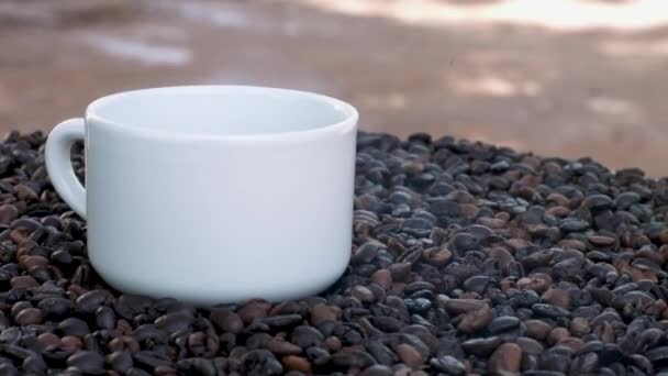 Szoros kilátás pörkölt kávébab és egy csésze kávé - Felvétel, videó