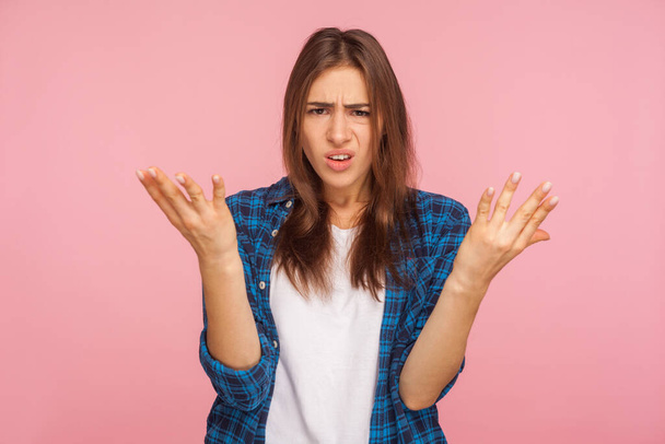 What do you want? Portrait of annoyed girl in checkered shirt raising arms in questioning gesture, saying I don't understand problem, looking indignant. indoor studio shot isolated on pink background - Photo, image