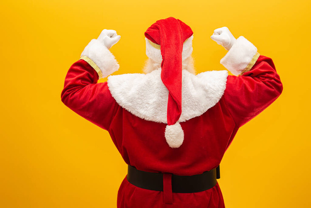 Santa Claus on his back on yellow background. Santa Claus from behind, looking back. - Photo, Image