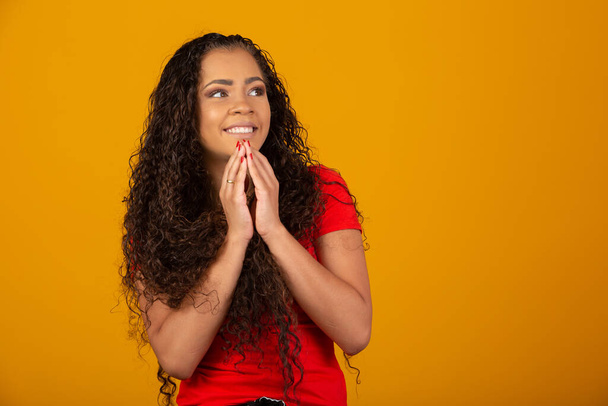 Beautiful African American woman with hands together in praying gesture, expressing hope and please concept. Brazilian curly hair girl. - Photo, Image