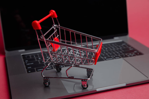 Online vásárlás koncepció. Laptop és kis kosár a rózsaszín háttér. - Fotó, kép