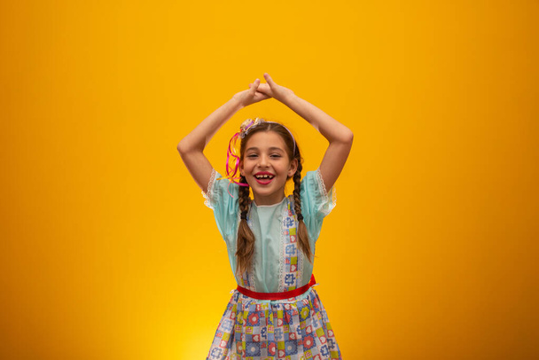 Child in typical clothes of famous Brazilian party called "Festa Junina" in celebration of So Joo. Beautiful girl on yellow background - Foto, imagen