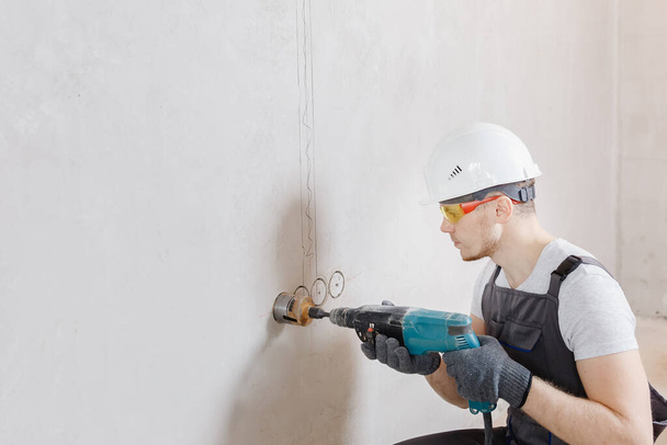Рабочий пневматический молоток строитель сверлит отверстие в бетонной кирпичной стене с алмазной короной для электрического кабеля, розетки, выключателя - Фото, изображение