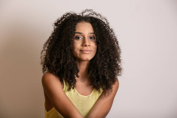 Νεαρή Αφρο-Αμερικανίδα με σγουρά μαλλιά που κοιτάει την κάμερα και χαμογελάει. Χαριτωμένο afro κορίτσι με σγουρά μαλλιά χαμογελώντας κοιτάζοντας κάμερα. - Φωτογραφία, εικόνα