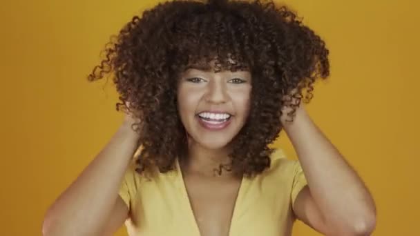 Young brazil curly woman gesturing and posing on yellow background - Кадри, відео