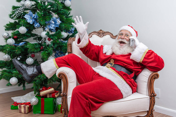 Santa Claus usando un teléfono inteligente. Hablando por teléfono con un niño. Analizar las solicitudes de Navidad
. - Foto, imagen