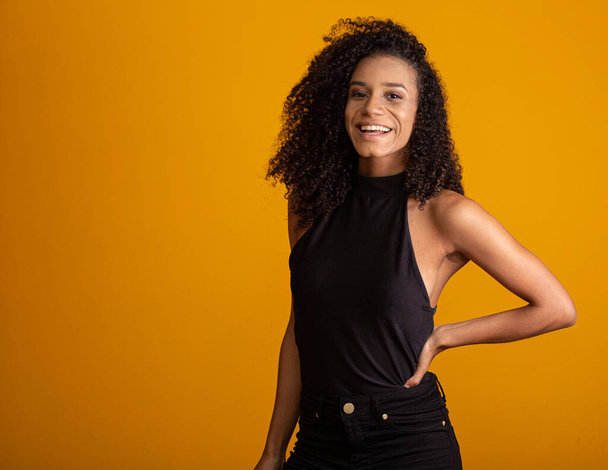 Young afro-american woman with curly hair looking at camera and smiling. Cute afro girl with curly hair smiling looking at camera. - Foto, afbeelding