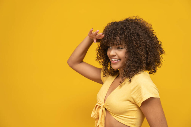 Junge lateinisch gelockte Frau posiert auf leuchtend gelbem Hintergrund - Foto, Bild