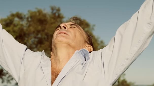 Зрелый мужчина поднимает руки в воздухе, наслаждаясь солнечной погодой
 - Кадры, видео
