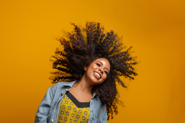 Гарний портрет афро-американки з зачіскою і гламурною гривою. Бразилька. Змішана раса. Кучеряве волосся. Стиль волосся. Жовтий фон. - Фото, зображення