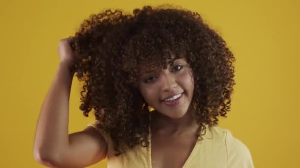Young brazil curly woman gesturing and posing on yellow background - Materiał filmowy, wideo