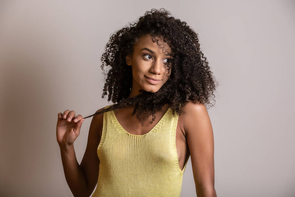 Young afro-american woman with curly hair looking at camera and smiling. Cute afro girl with curly hair smiling looking at camera. - Photo, image